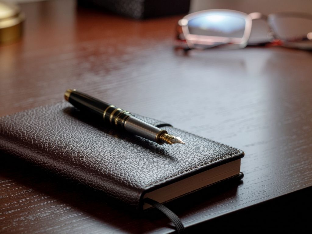 A fountain pen resting on a leather notebook on an executive desk